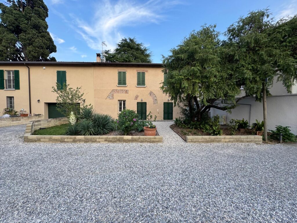 Corte d’ingresso dopo l’intervento: aiuole con contorni in corten e tufo, prato in zoysia, ghiaia riordinata